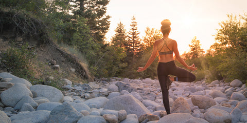 Woman doing a yoga pose on a rocky hill side.